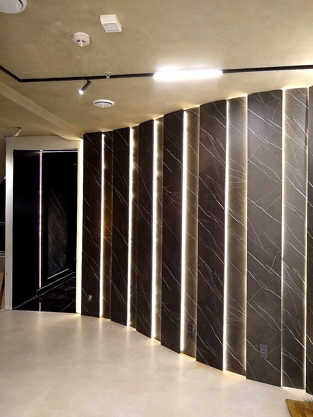 Parede curva revestida em mármore com iluminação embutida